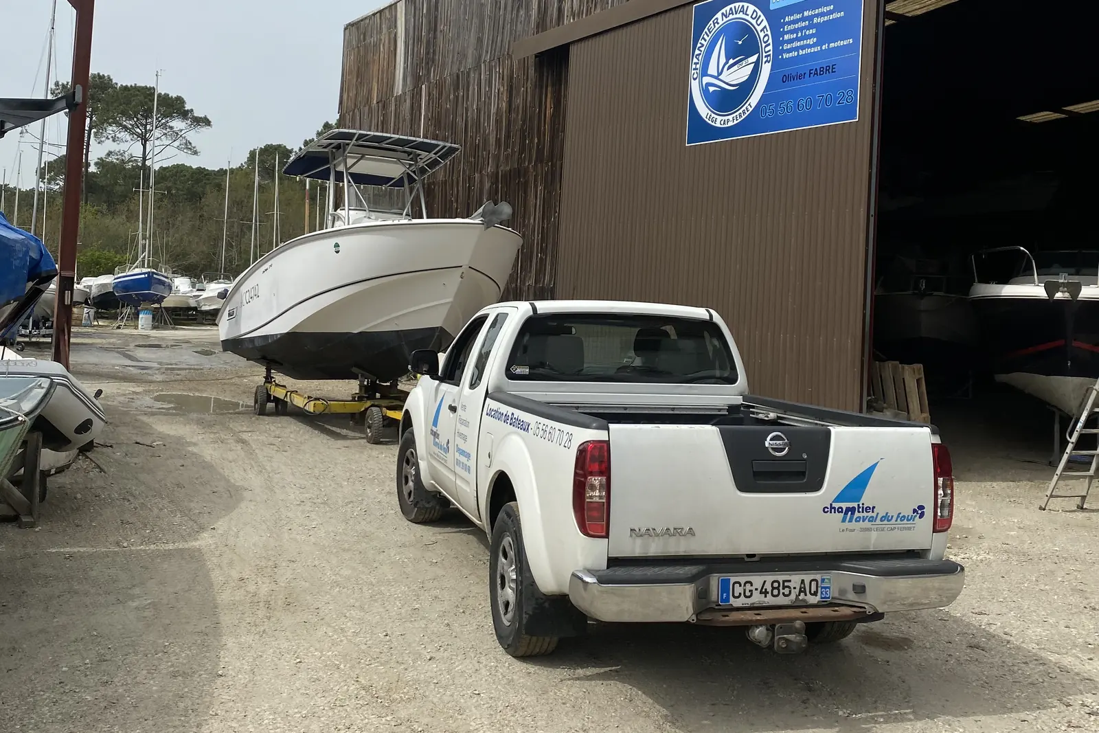 le hangar du chantier, son panneau et le pick-up, un bateau sur sa remorque